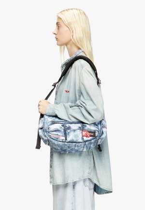 Schultertasche im Denim-Muster mit verstellbarem schwarz-weißem Schulterriemen, ausgestattet mit zwei Fronttaschen und einem roten Logopatch auf blauer Basis.
