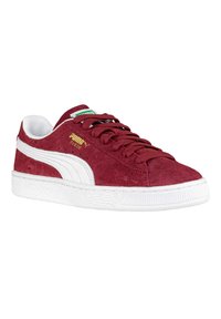 Sneaker rossa in suede con dettagli bianchi, suola in gomma testurizzata e design a strisce bianche di Puma. Presenta una punta arrotondata e chiusura con lacci.