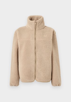 Chaqueta de forro polar beige con cuello alto, cremallera frontal y puños elásticos. Textura suave con apariencia ligeramente esponjosa.