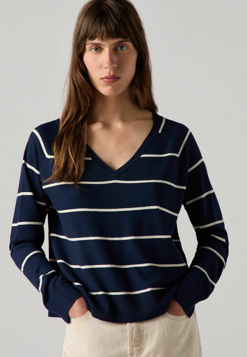 Pull rayé bleu marine avec des rayures horizontales blanches, décolleté en V, manches longues et ourlet côtelé. Tissu en tricot doux avec une coupe décontractée.