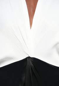 Mustvalge kleit sügava V-kaelusega, millel on plekitud valge kangas ülaservas ja sile must kangas koos seotud detailiga talje kohal.