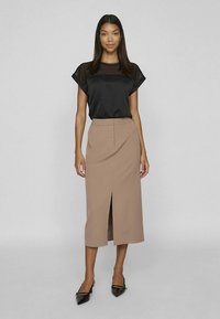 Svart kortermet topp med gjennomsiktig overlegg kombinert med en beige blyantskjørt til kneet med frontsplitt. Svarte spisse sko.