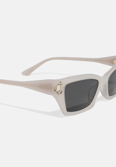 Sunglasses with a translucent light pink frame, dark lenses, and a gold accent logo on the front near the hinge. Square design.