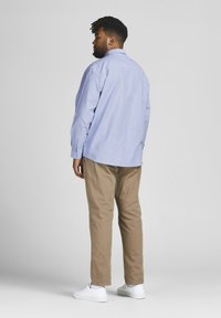 Hellblaues Hemd mit Knöpfen, khakifarbene Hose und weiße Sneakers. Das Hemd hat lange Ärmel und eine lockere Passform mit einer glatten Textur.