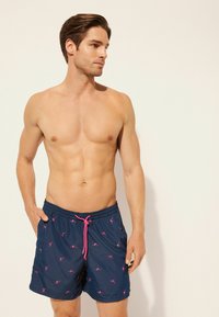 Bañador en color azul marino, con un diseño de flamencos en color rosa. Material ligero con una cintura elástica y cordón ajustable.
