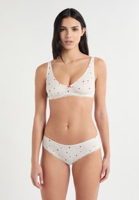 Beiges, geripptes Dessous-Set mit kleinen roten Herzmustern, Spitzenbesätzen und weicher Textur für Komfort. Enthält ein dreieckiges Bustier und einen Slip.