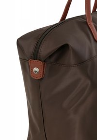 Borsa di stoffa marrone con una superficie liscia, dotata di una cerniera superiore e dettagli in pelle marrone. Un bottone in metallo appare sul lato.