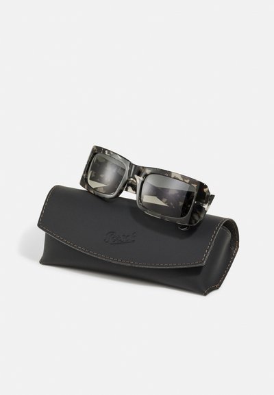 Ochelari de soare pătrați cu un model de camuflaj în nuanțe de gri, așezați pe un toc din piele neagră cu accente cusute și un logo.