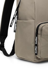 Grå tygryggsäck med slät textur, två dragkedjor med svarta draglappar och justerbara svarta nätremmar.