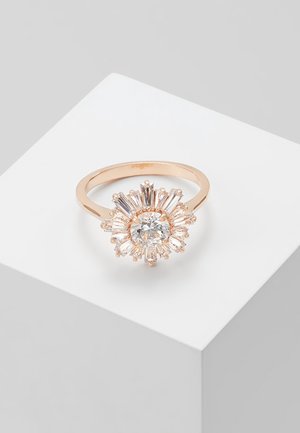 Roségoldring mit einem runden zentralen klaren Edelstein, umgeben von baguettegeschliffenen Steinen in einem Sonnenstrahldesign, auf einem weißen Podest präsentiert.