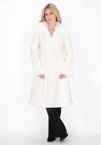 White coat with a fur collar and cuffs, featuring a wide design and textured trim. Worn over black pants and black boots.