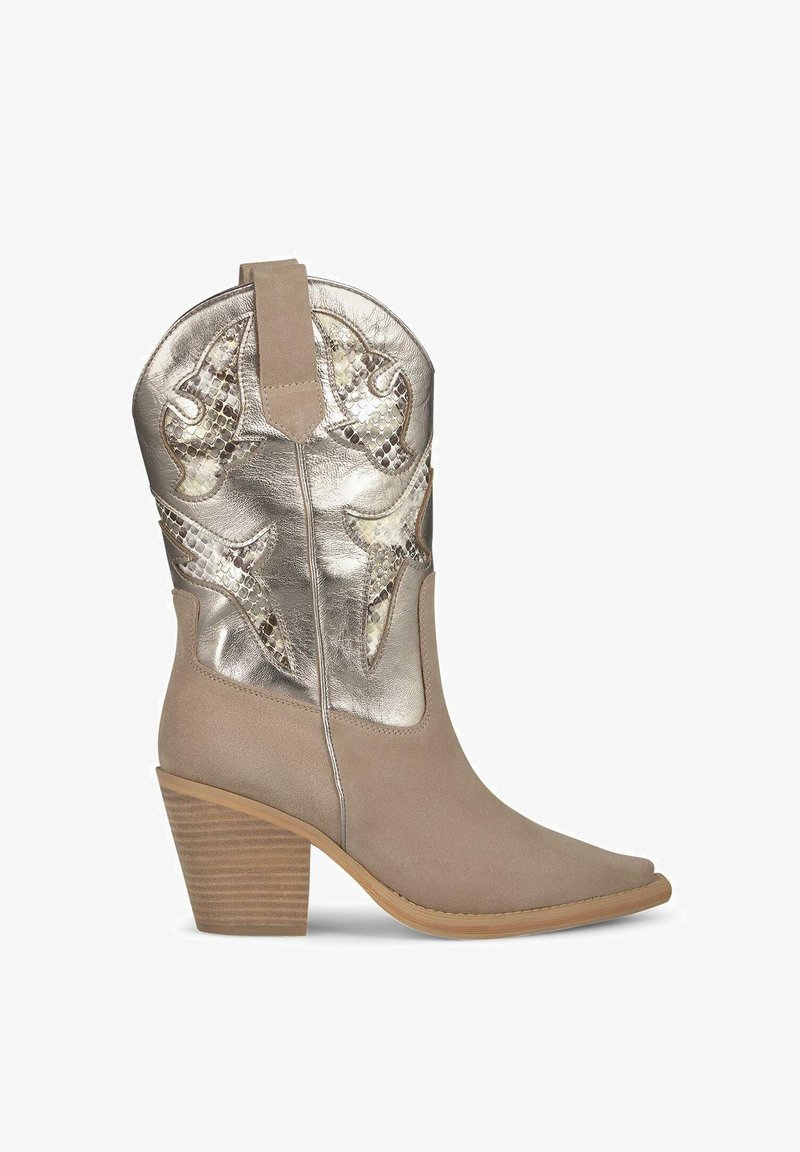Bottine de cowboy en daim beige avec des accents métalliques argentés, pointe effilée et talon en bois empilé, ornée d'un motif de couture décoratif.