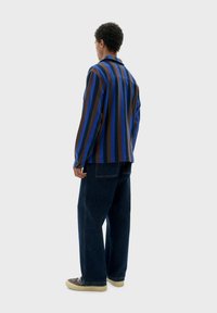 Gestreepte blouse met lange mouwen in blauw en bruin, gecombineerd met donkere denimbroek. De blouse heeft een relaxte pasvorm en manchetten met één knop.