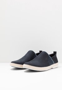 Scarpe slip-on navy con texture scamosciata liscia, pannelli laterali elastici e suola in stile juta intrecciata. Presentano un'etichetta sul tallone.