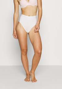 Fundo branco de alta cintura com uma textura suave, apresentando um design sem emendas e um corte clássico, complementando um sutiã rosa acolchoado.