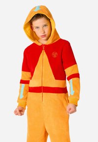 Fliisist kombinesoon kapuutsi, oranži ja punase värvusega, siniste noolemärkidega varrukatel ning ümmarguse logoga rinnal. Lukuga sulgemine.