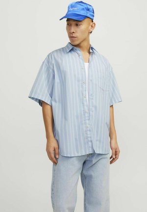 Camisa de manga corta de botones azul claro con rayas verticales, combinada con jeans de mezclilla azul claro y una gorra azul. Presenta un bolsillo en el pecho.