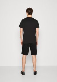 T-shirt en coton noir à manches courtes, associé à un short noir. Le tissu semble lisse et le design est simple et minimaliste.