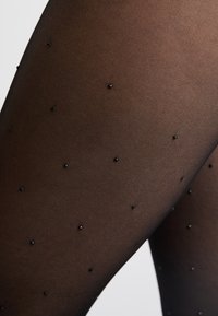 Collant neri trasparenti con un motivo testurizzato, decorati con piccole perline nere per un accento e un interesse visivo. Finitura liscia.