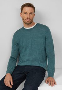 Turkusowy sweter z długim rękawem, wykonany z miękkiego, teksturowanego splotu; okrągły dekolt; nałożony na biały t-shirt; noszony z ciemnymi dżinsami.