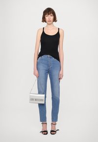 Fekete ujjatlan felső, világoskék egyenes lábú farmernadrág, ezüst kézitáska "LOVE MOSCHINO" felirattal, fekete szandál masnikkal, a modellt középen állva.