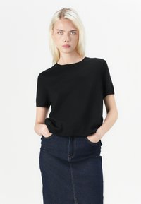Chemise noire à manches courtes avec un col arrondi, en tissu doux. Associée à une jupe en denim foncé taille haute.