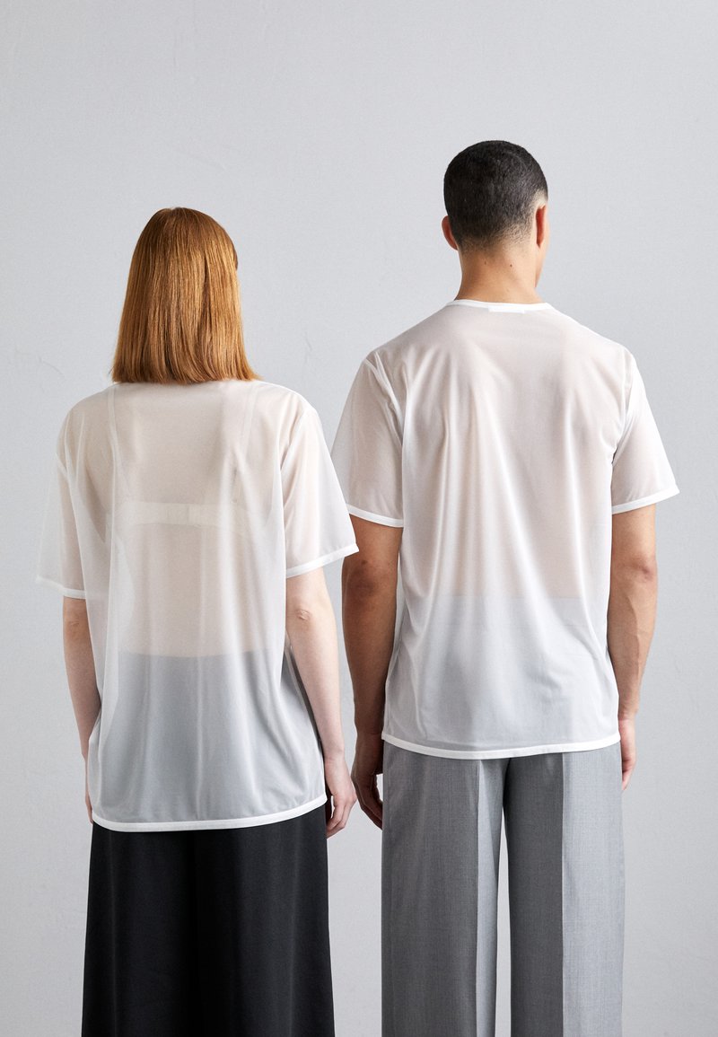 Weiße, durchsichtige T-Shirts mit kurzen Ärmeln und Rundhalsausschnitten, die einen subtilen Farbverlauf zum Saum hin aufweisen. Kombiniert mit kontrastierenden Hosen.