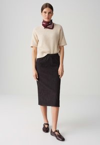 Top corto a maniche corte in misto lana beige, gonna a tubino nera a costine, sciarpa a motivo bordeaux, e scarpe marroni con dettaglio a fibbia.