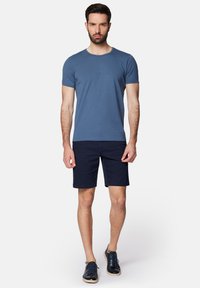 Niebieska bawełniana koszulka z okrągłym dekoltem, w zestawieniu z ciemnonawigacyjnymi szortami. Uzupełnieniem stroju są casualowe granatowe buty.