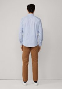Camisa de manga larga azul claro con cuello abotonado, combinada con chinos marrones y zapatillas blancas, vista desde la parte trasera.