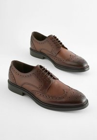 Pantofi de dress din piele maro cu un design brogue, având perforații, vârf ascuțit și talpă din cauciuc negru.