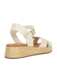 Beige wedge sandaal met geweven jute platform, kruislings banden, veilige gesp en een gladde lederen textuur. Zijkant, semi-open ontwerp.