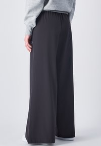 Schwarzweite Hosen aus leichtem Stoff mit einem elastischen Bund und einem kleinen Logopunkt an der Seite. Glatte Textur ohne Muster.