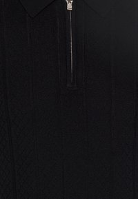 Černý pletený polo svetr se zipem, se strukturovaným vzorem a žebrovaným límcem. Má vertikální pruhy a jemný lesk.