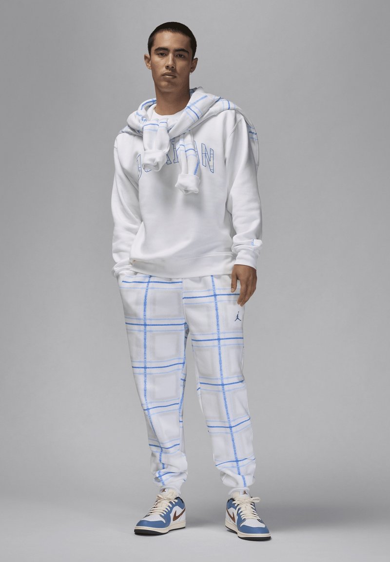 Haut à capuche blanc avec le lettrage bleu "JORDAN", associé à un pantalon de survêtement blanc avec un motif à carreaux bleu. Baskets blanches avec des accents bleus.