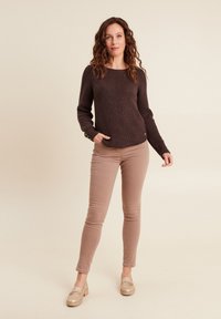 Brauner gestrickter Pullover mit strukturiertem Muster, rundem Ausschnitt und langen Ärmeln. Kombiniert mit hellbeigen Slim-Fit-Hosen und beige-farbenen Mokassins.