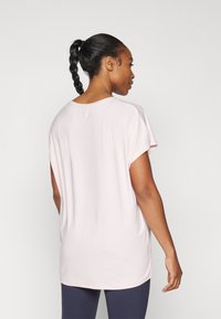 Light pink loose-fit T-shirt with short sleeves, round neckline, soft texture, and extended back hem. Direct view from the back.