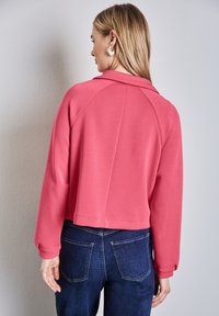 Fuchsian kort jacka med långa ärmar och krage. Slät, mjuk tyg med en avslappnad passform, kombinerad med mörk denimjeans.