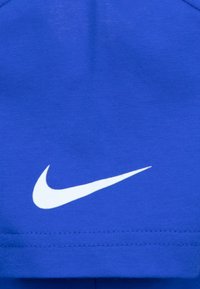 Kráľovsky modré športové tričko z hladkej tkaniny. Vyznačuje sa výrazným bielym logom Nike a krátkymi rukávmi. Detail šitia viditeľný na leme.