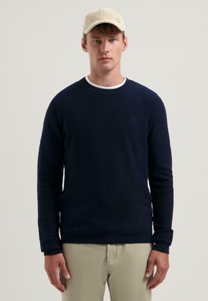 Marineblauwe, crew-neck trui met een textuurbrei en geribde manchetten. Gecombineerd met een lichtgekleurde katoenvelours pet. Eenvoudig, casual ontwerp.