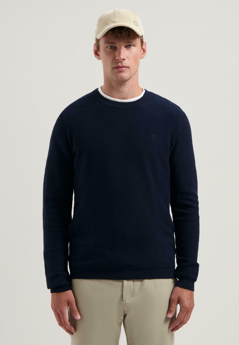 Dunkelblaues, Rundhalsausschnitt Sweatshirt mit strukturiertem Strick und gerippten Bündchen. Kombiniert mit einer hellen Cordmütze. Schlichtes, lässiges Design.