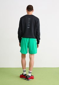 Hanorac negru cu logo-ul "NIKE" pe spate, asortat cu pantaloni scurți verzi aprinși, pantofi negri și roșii și șosete cu dungi albe.