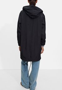 Czarna bluza z kapturem o luźnym kroju, długich rękawach, i sznurkiem u dołu, wykonana z gładkiego materiału; w połączeniu z jasnoniebieskimi szerokimi spodniami.