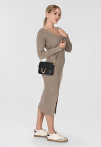 Abito color cammello a coste, lungo fino al ginocchio, con maniche lunghe e spacco laterale, abbinato a una borsa a spalla nera con hardware dorato e sneakers bianche.