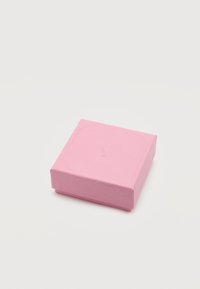Μικρό κλειστό ροζ κουτί δώρου με υφή και διακριτική ανάγλυφη σφραγίδα στο καπάκι, τοποθετημένο σε λευκή επιφάνεια.