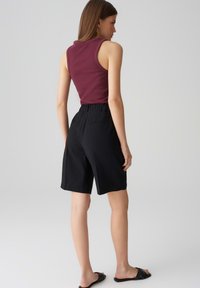 Pantaloni corti neri con vita elastica, abbinati a una maglietta senza maniche color bordeaux. Tessuto liscio, design casual e silhouette semplice.