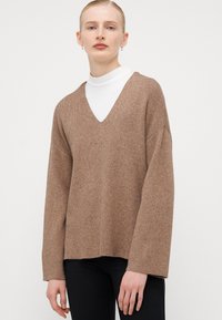 Brauner, übergroßer Pullover mit tiefem V-Ausschnitt, aus einem weichen Wollgemisch. Mit langen Ärmeln mit Rippstruktur und geradem Saum.