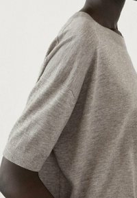 Harmaa lyhythihainen neule pehmeästä trikookudoksesta, jossa on rennon leikattu malli ja ribbireunat. Yksinkertainen, saumatonta muotoilua, jossa on pyöreä kaula-aukko.