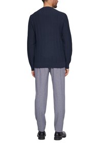 Granatowy sweter dzianinowy z teksturowanym, prążkowanym wzorem, zestawiony z jasnoszarymi, luźnymi spodniami i czarnymi butami, widok z tyłu.