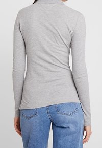 Gray long-sleeve top with a collar, made of soft fabric. Features a fitted design with a slightly curved hem, paired with high-waisted blue jeans.
